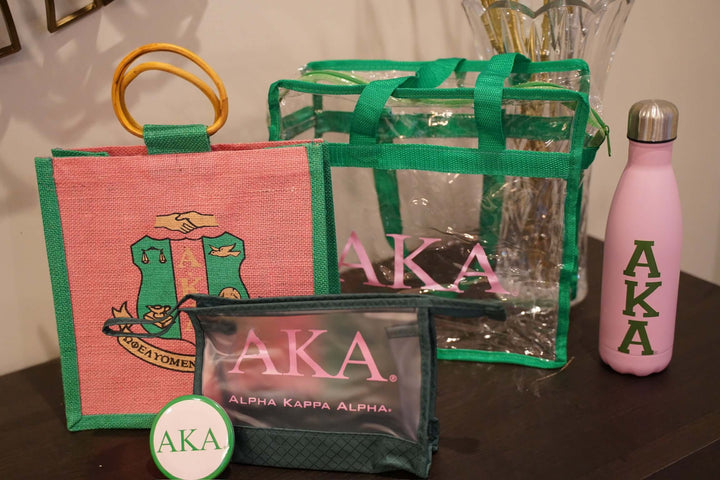 Collection of AKA sorority bags and a water bottle featuring Greek gear and paraphernalia on a table.