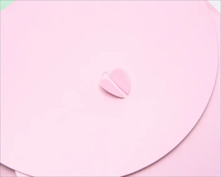 Close-up of a pink heart-shaped embellishment on a soft pink background, perfect for unique gift wrapping.