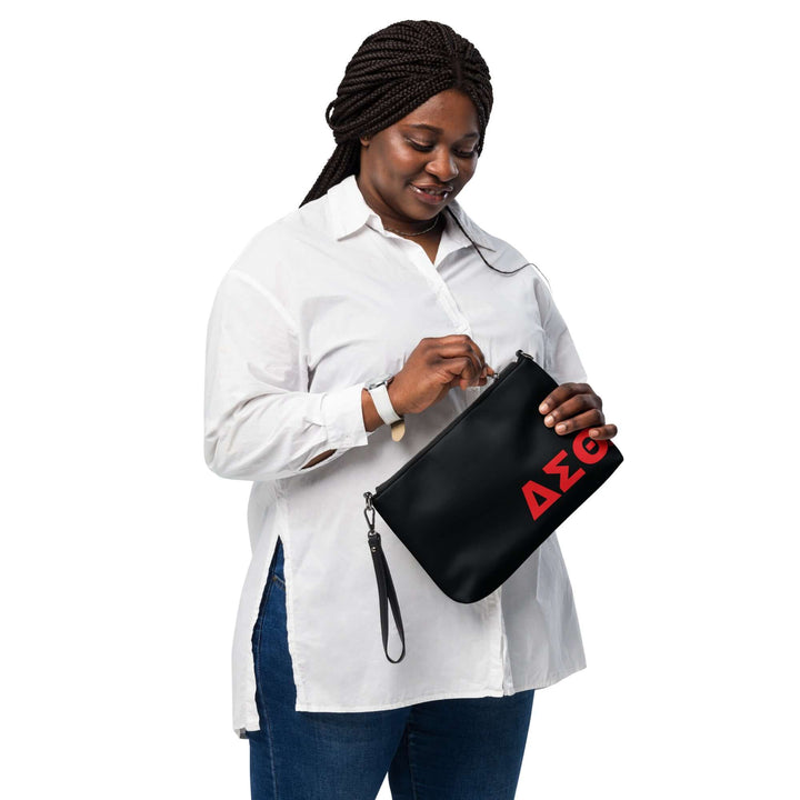Woman wearing a white shirt, holding a Delta Sigma Theta Sorority crossbody bag with a bold logo, showcasing Greek gear style.