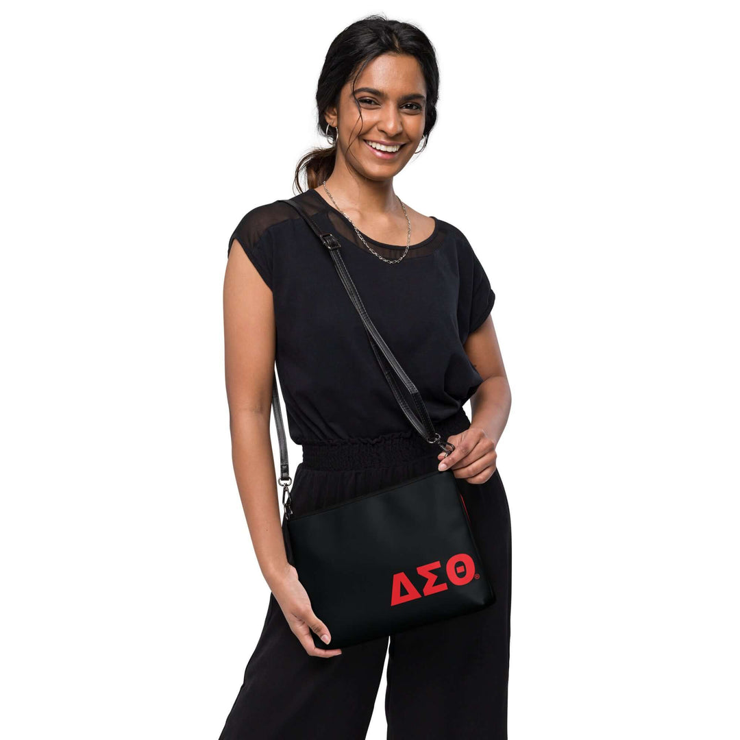 Woman wearing a black outfit, posing with a Delta Sigma Theta Soror crossbody bag featuring red Greek lettering.